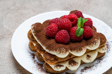 portion of Classic tiramisu dessert with raspberries on grey concrete background