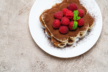 portion of Classic tiramisu dessert with raspberries on grey concrete background