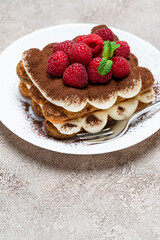 portion of Classic tiramisu dessert with raspberries on grey concrete background