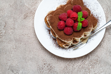portion of Classic tiramisu dessert with raspberries on grey concrete background
