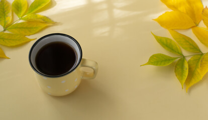 A cup of black tea in a ceramic yellow cup with autumn leaves on a yellow background. Selective focus. Horizontal orientation.