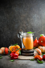 Pumpkin soup in a transparent jar on a table with autumn vegetables. Harvest tomatoes, pumpkins and peppers.