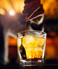The bartender stirs a spoonful of whiskey with ice in a glass.