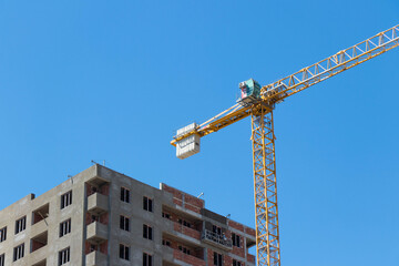 Building crane and buildings under construction against blue sky. Industrial theme
