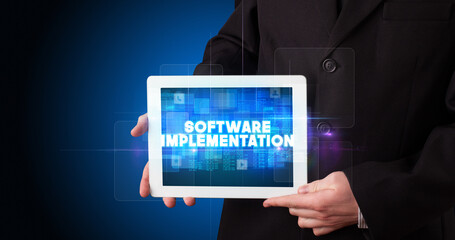 Young business person working on tablet and shows the inscription: SOFTWARE IMPLEMENTATION