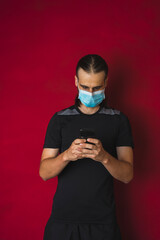 Man with mask watching mobile with gym sportswear on red background - COVID 19