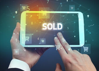 Close-up of a hand holding tablet with SOLD inscription, online shopping concept
