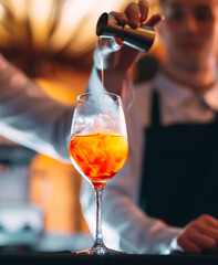 Barman hand stirring a fresh and sweet orange summer cocktail with a spoon on the bar counter.