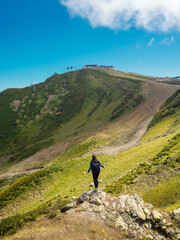 tourist stands on one peak and looks into the distance at a higher mountain.