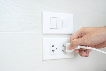 Closeup Male finger unplugging or plugging of electricity device on white wall at home. Energy Saving, power, electrical and lifestyle concepts