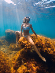 Woman in posing at rock underwater. Free diver relax in blue sea