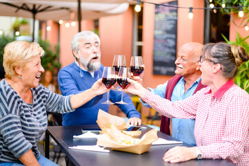 Happy senior friends smiling  and toasting red wine at bar