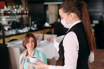 A European-looking waiter in a medical mask serves coffee.
