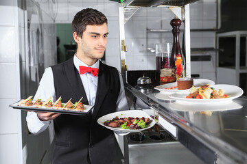 The waiter with the ready prepared dishes in the restaurant kitchen.