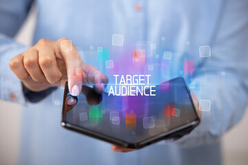 Young man holding a foldable smartphone with TARGET AUDIENCE inscription, educational concept