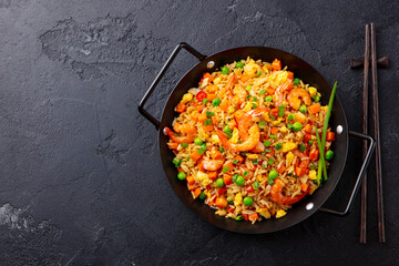 Stir fry rice with vegetables and shrimps in black iron pan. Slate background. Copy space. Top view.