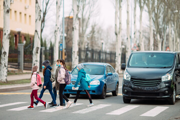 School children cross the road in medical masks. Children go to school.