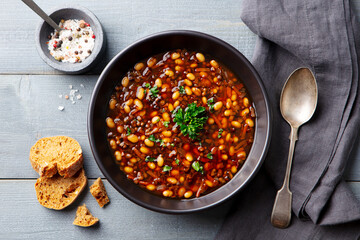 Bean soup in a black bowl. Grey wooden background. Close up. Top view.