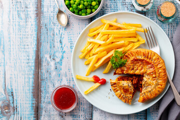 Meat pie with french fries on a white plate. Wooden background. Copy space. Top view.