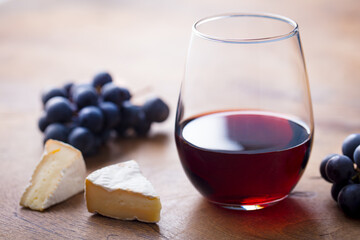Glass of red wine with fresh grape and cheese on wooden table. Close up.