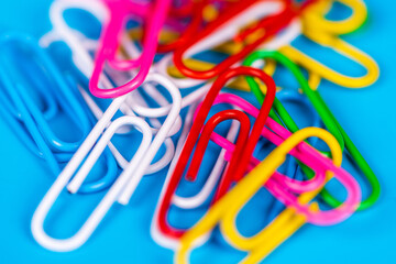 Heap of colorful paper clips with blurred blue background.