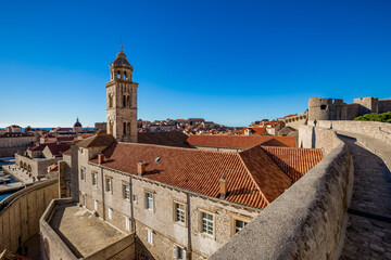 Fototapeta na wymiar Colorful fortress street walk scene, clear sky sunny day. Church bell tower, building roofs. Winter view of Mediterranean old city Dubrovnik, famous European travel and historic destination, Croatia