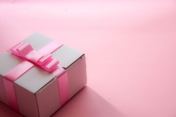 White gift box with a pink ribbon on a pink background.