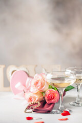 Champagne glasses, a bouquet of roses and a gift on a bright background. Romantic celebration of Valentine's day