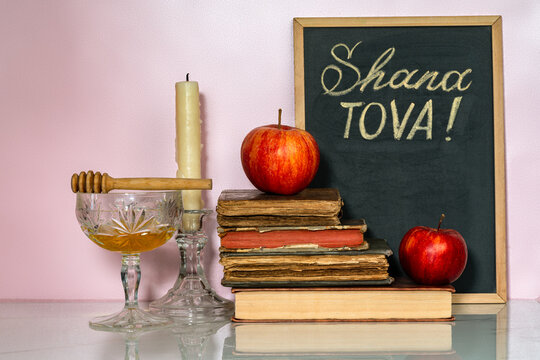 Hebrew inscription Good year (Shanah tovah) on a chalk board. Apples, pomegranates, candle and honey on white table.