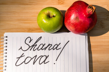 English written shana tova that is Happy Holidays next to pomegranate and apple. Jewish holiday called Rosh Hashanah.