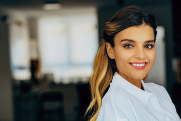 Portrait of a young woman smiling in front of window, wearing white blouse