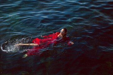 woman swims in the sea in a red long dress with sunglasses