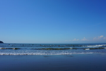 People surfing on sea waves under blue sky. Katase Nishihama beach is one of Japan's most popular beaches