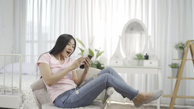 A happy, carefree young woman dancing happily alone sitting on a chair At home listening to beautiful music, active young women, jumping in the bedroom, enjoying freedom and way of life.
