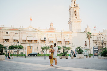 A girl in a hat and a dress with a plunging neckline is dancing with her boyfriend with a beard and sunglasses in the old town. A couple of tourists on the sunset in Valencia.