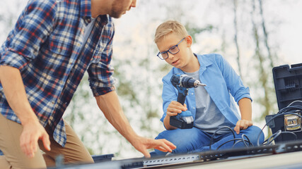 Father and Son Installing Solar Panels to a Metal Basis. Son Passes Drill to a Father. They Work on a House Roof on a Sunny Day. Concept of Ecological Renewable Energy at Home and Quality Family Time.