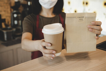 waitress wearing protection face holding hot coffee cup and paper bag waiting for customer in...