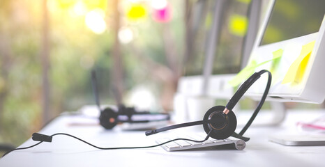 VOIP headset on desk with computer desktop at customer service and marketing support workplace. Office supplies of customer service. Communication support, call center and helpline concept.