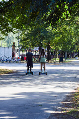 A guy and a girl ride a hoverboard with their backs in the park and hold hands