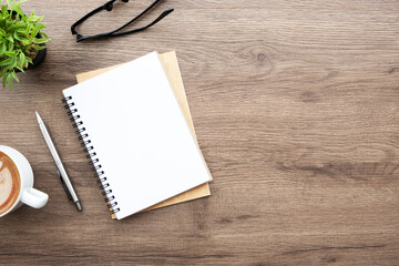 Blank notebook with pen are on top of wood office desk table with cup of latte coffee and supplies....