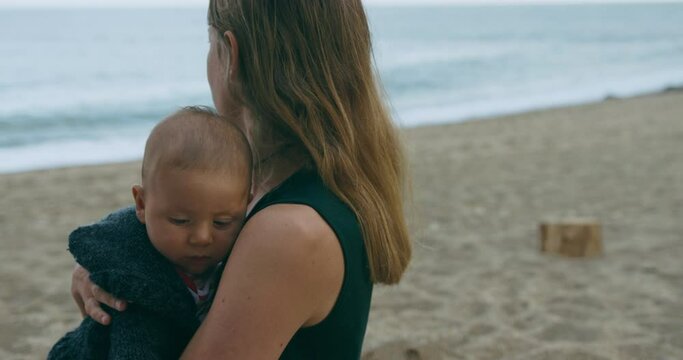 A little baby on the beach is being sick over his mother