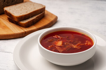 Vegetarian borscht in a white tureen on a light wooden table near pieces of bread