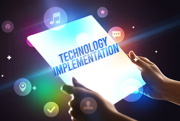 Holding futuristic tablet with TECHNOLOGY IMPLEMENTATION inscription, new technology concept