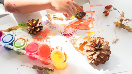 Toddler boy is home schooled paiting yellow leaves and pine cones in fall with eco friendly paint....