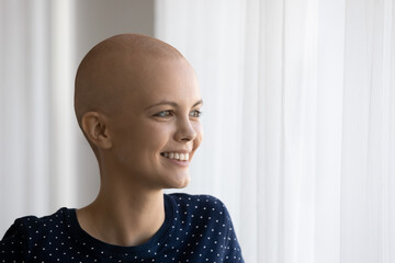 Close up of smiling young hairless woman struggle with oncology look in distance thinking or dreaming. Happy sick bald female patient with cancer feel positive optimistic with recovery or remission.
