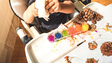 Toddler boy is home schooled painting yellow leaves and pine cones in fall with eco friendly paint. Sensorial activity at home.