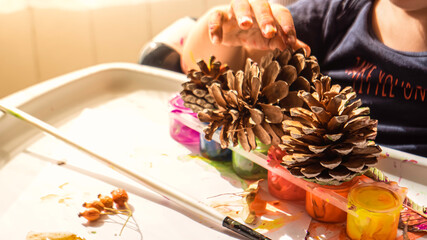 Toddler boy is home schooled paiting yellow leaves and pine cones in fall with eco friendly paint. Sensorial activity at home.