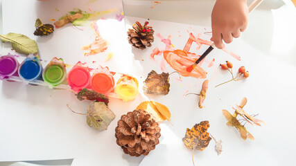 Toddler boy is home schooled paiting yellow leaves and pine cones in fall with eco friendly paint. Sensorial activity at home.