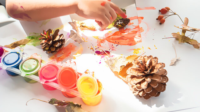 Toddler boy is home schooled paiting yellow leaves and pine cones in fall with eco friendly paint. Sensorial activity at home.