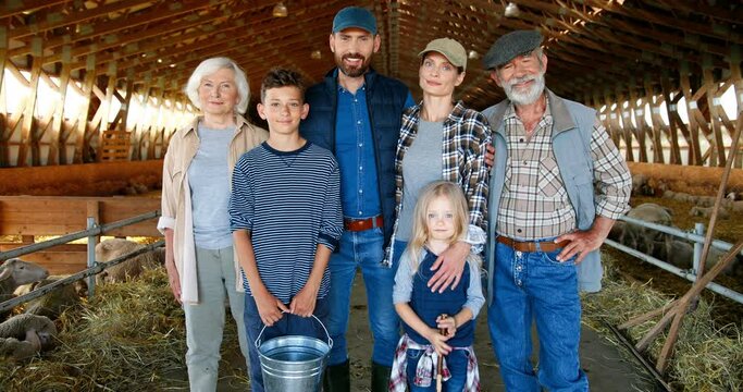 Portrait of happy Caucasian family of three generations standing in shed with livestock and smiling. Old parents with children and grandchildren in barn. Farmers, kids at farm. Zooming in. Dolly shot.